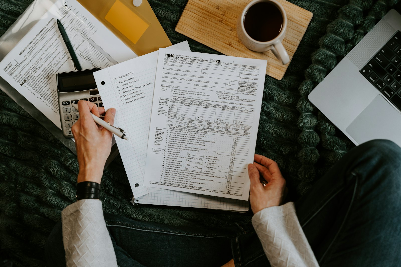 A person at home goes over financial paperwork with a pen, a calculator and a laptop.