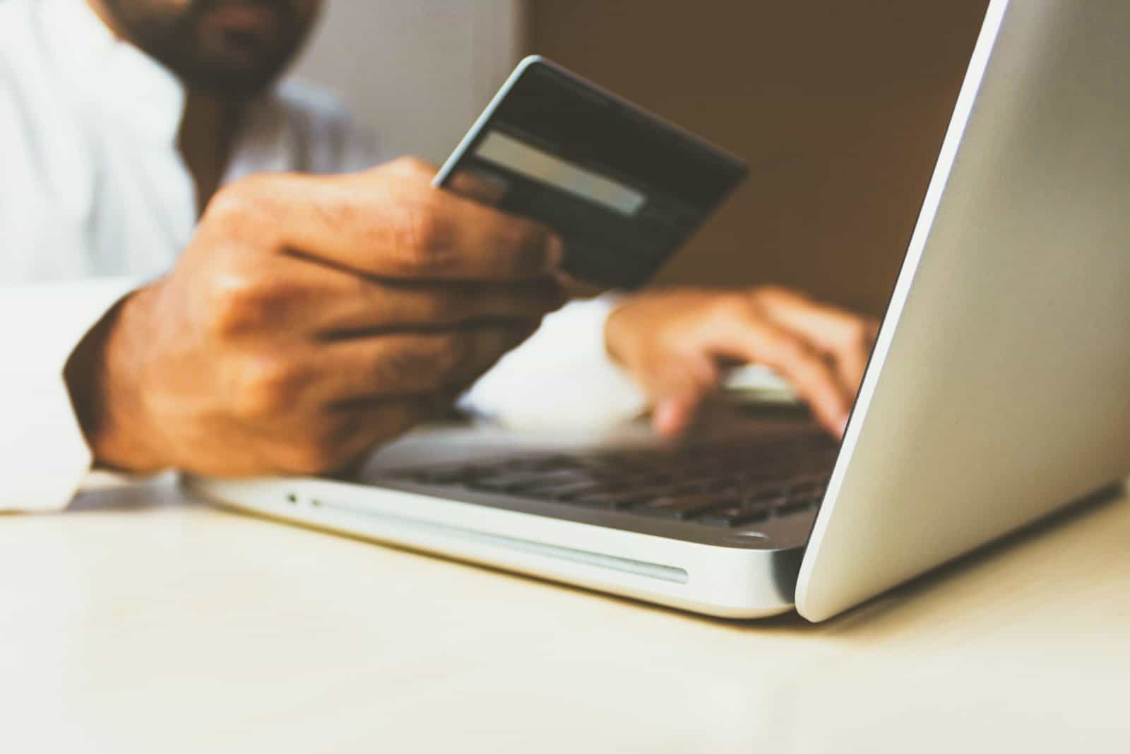 A person holding a credit card while using a laptop to manage an account online.