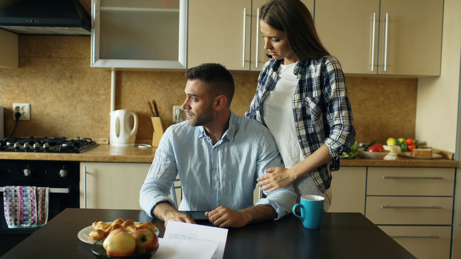 A couple sits at their kitchen table reviewing household bills and paperwork together.