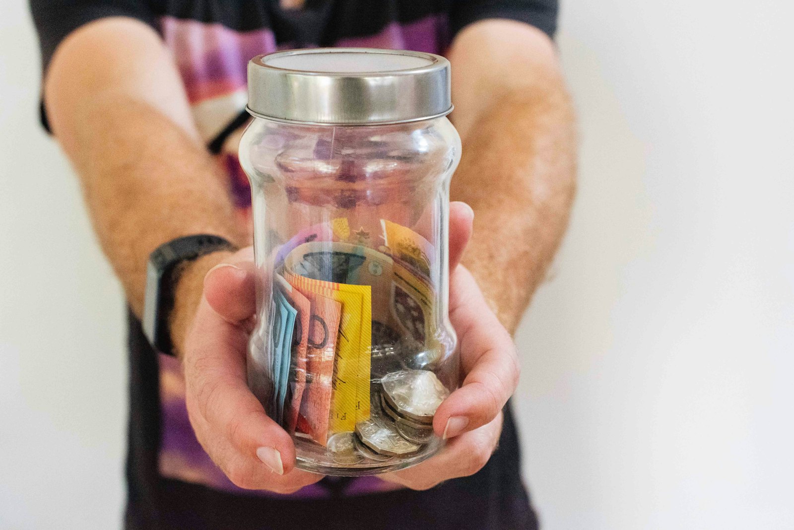 A person holds a clear glass jar filled with cash savings.
