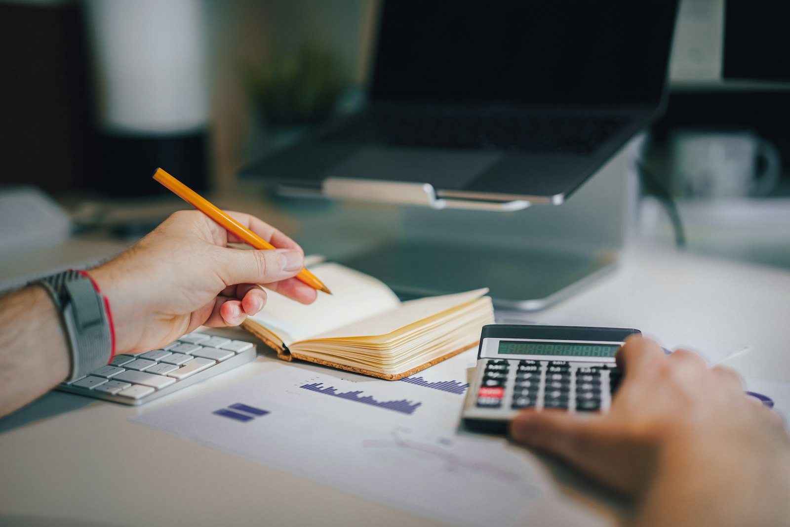 A person at a desk works through numbers with a calculator and a notebook