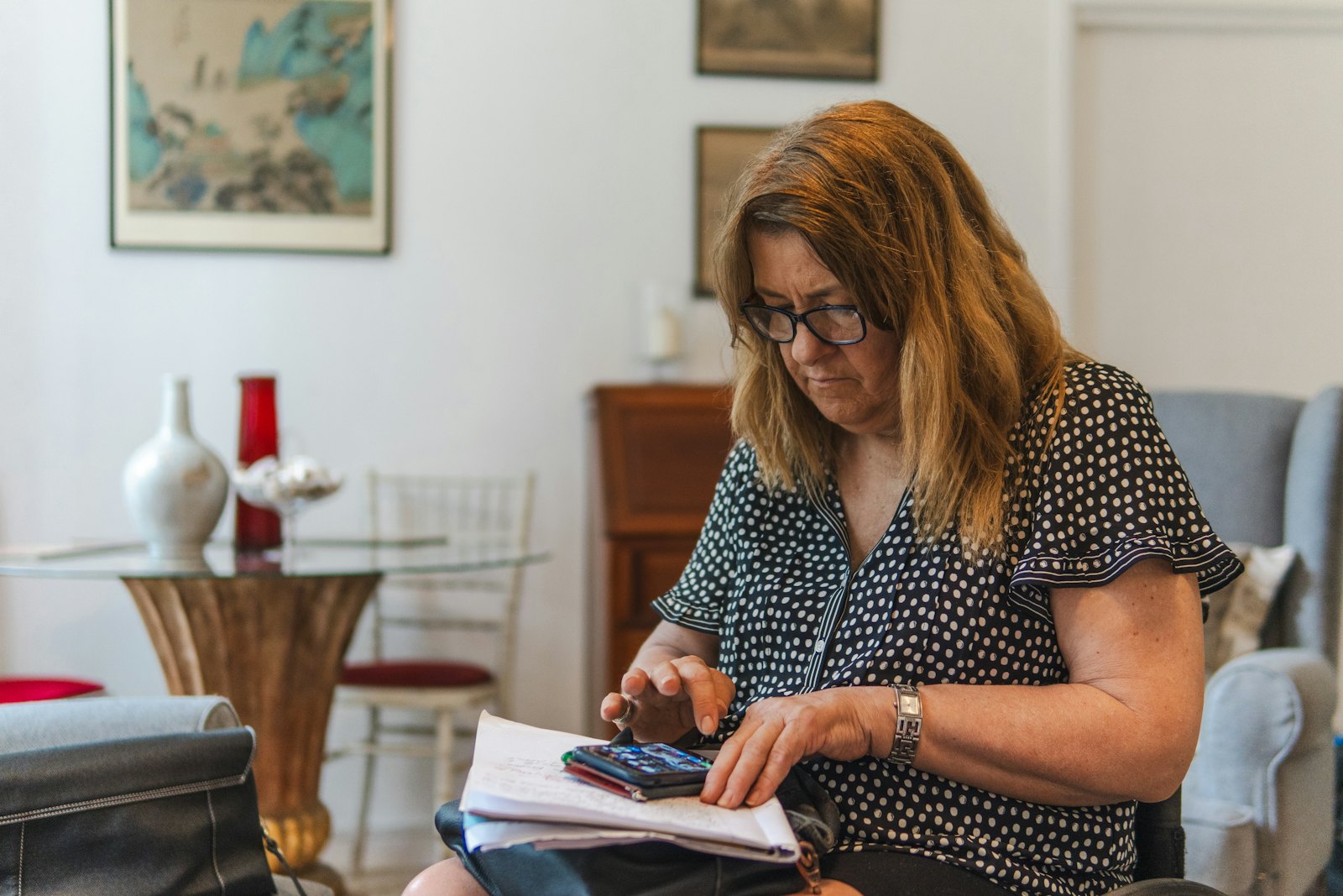 A woman sits at her dining table with a calculator and a stack of bills, working out her monthly budget.