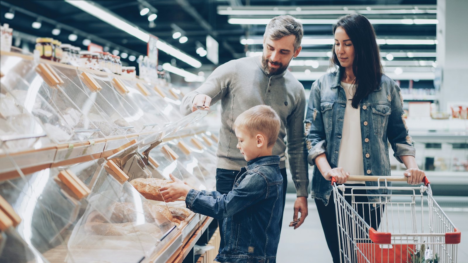 A father, mother, and young son shop for groceries together at a supermarket, picking items from the shelves.