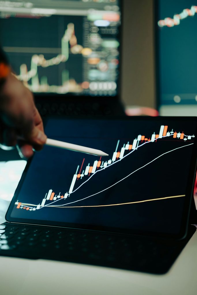 A person points at a market chart on a laptop screen while comparing investments