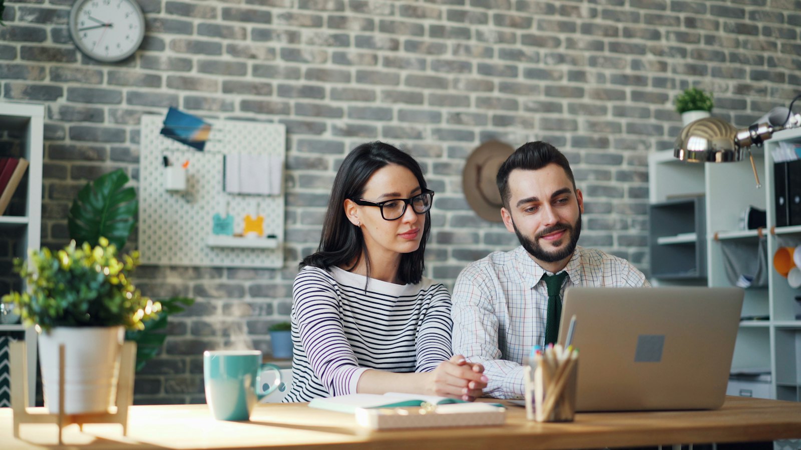 A man and a woman sit at a table looking at a laptop screen together