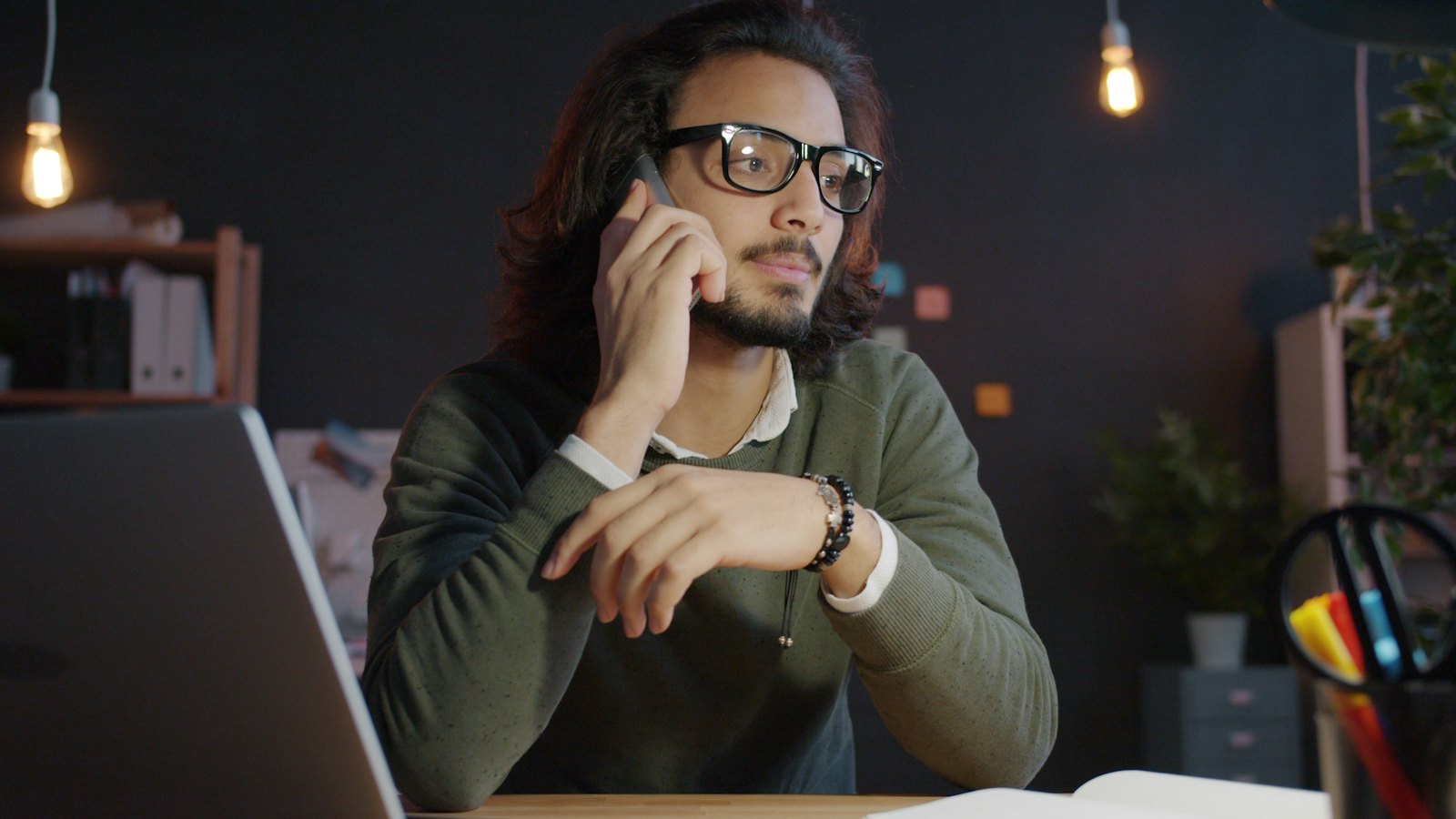 A man talks on the phone at a desk in the evening, the kind of call you might make to ask a company for a lower bill.