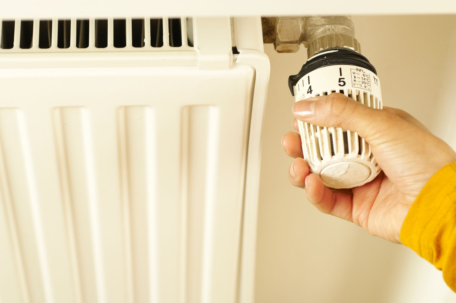 A close-up of a hand turning a radiator thermostat valve to adjust the home's heat.