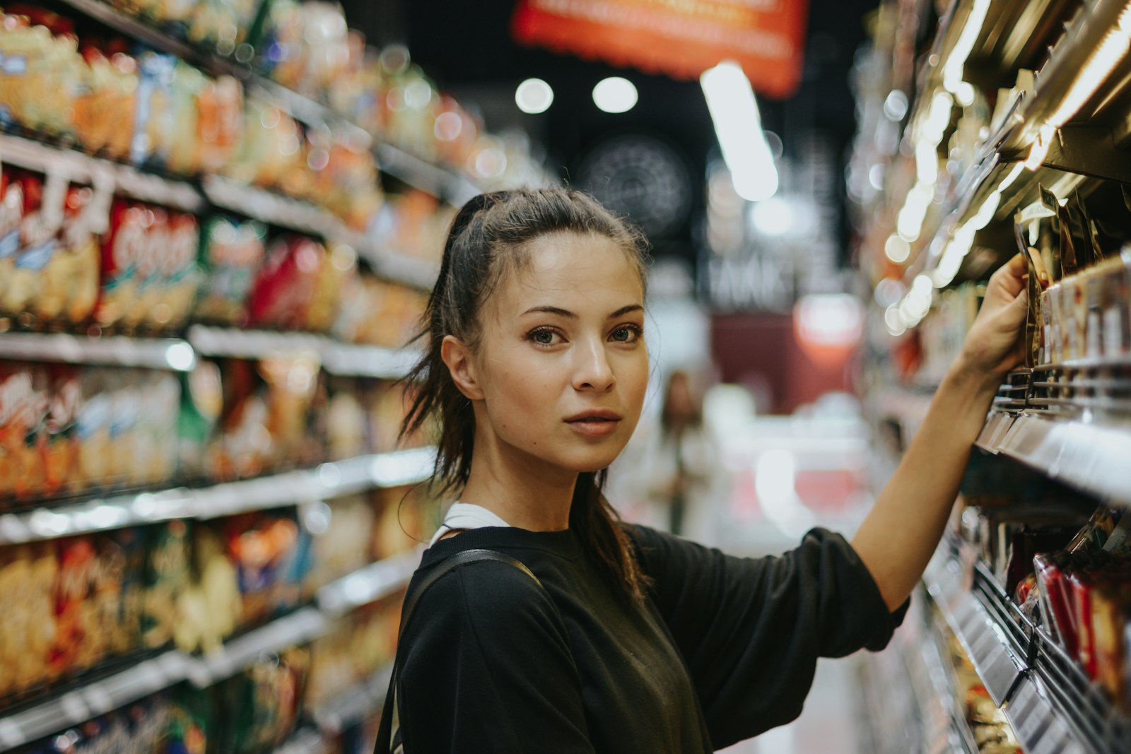 A woman browses the shelves in a grocery store aisle while shopping for food.