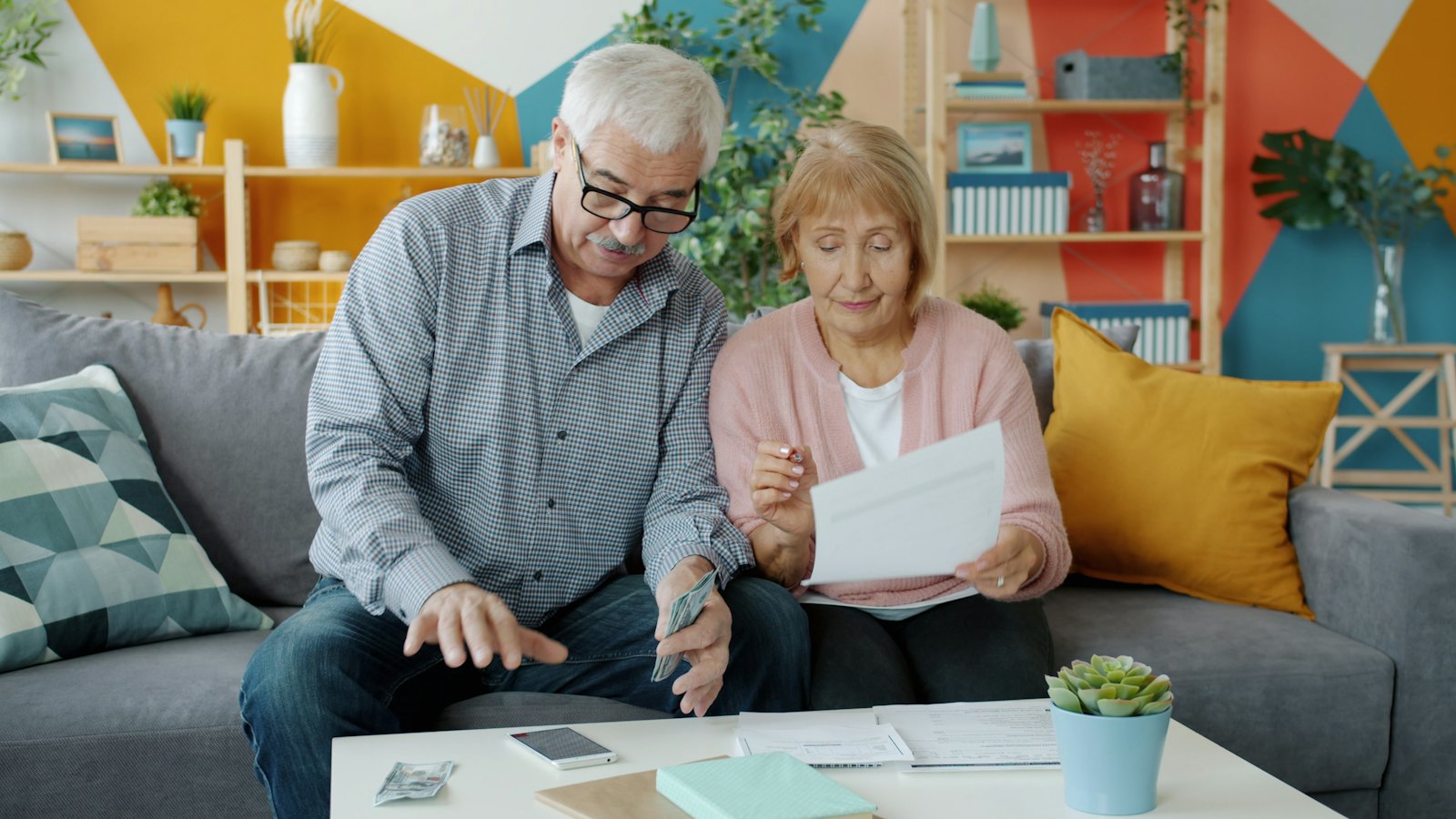 An older couple smiles as they count money and go over bills together at home.
