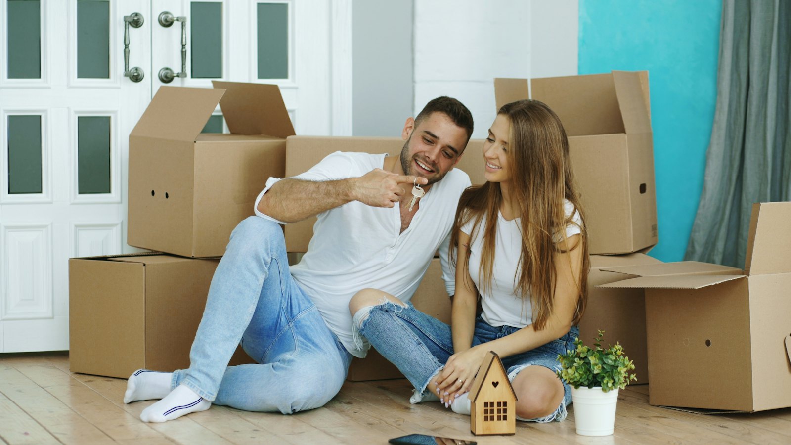 A happy young couple sitting on the floor among moving boxes in their new home, holding the keys